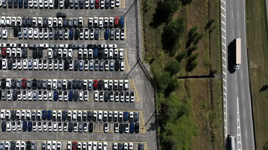 Imagem aérea de um estacionamento amplo lotado com diversos carros em fila, mostrando a organização e a variedade de veículos estacionados nas vagas.