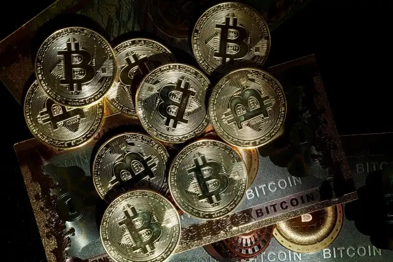 Imagem de várias moedas de Bitcoin em cima de notas representativas da moeda digital, destacando sua popularidade e valor no mercado financeiro.