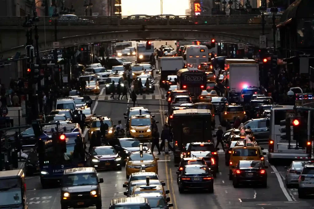 Vista movimentada da cidade com muitos carros e pessoas atravessando a rua, destacando o tráfego intenso e a vida urbana