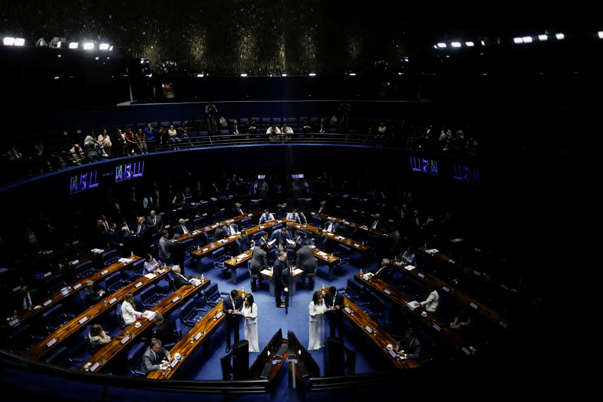 Imagem do plenário do Senado, com senadores discutindo e participando de uma sessão legislativa. O ambiente é grandioso e bem iluminado, refletindo a importância das deliberações políticas.