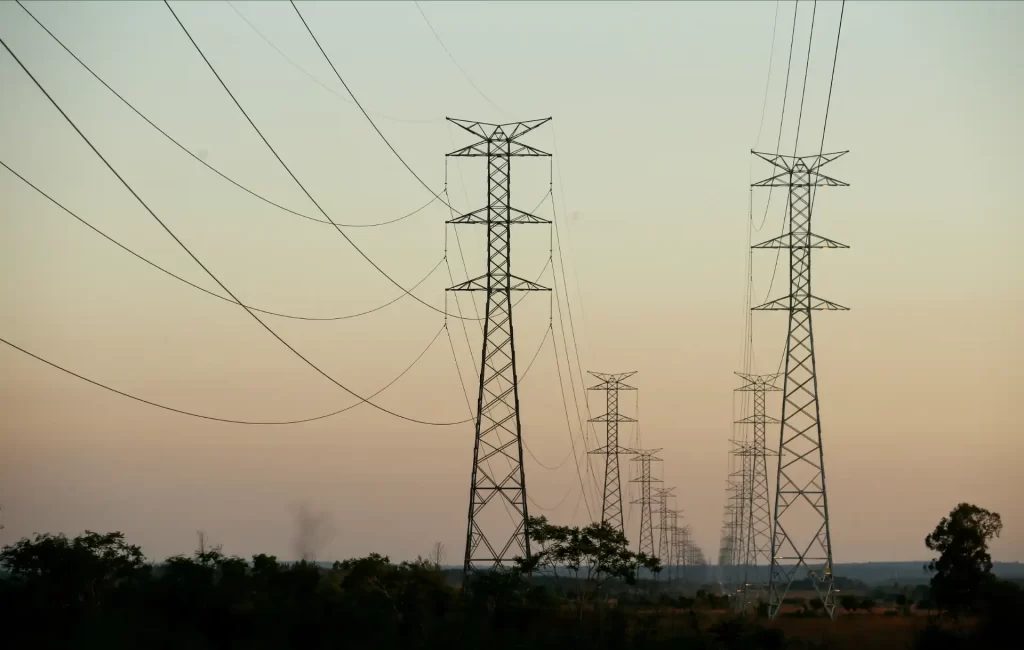 Imagem de torres de transmissão de energia elétrica em um campo aberto durante o pôr do sol, representando a infraestrutura de energia no Brasil.