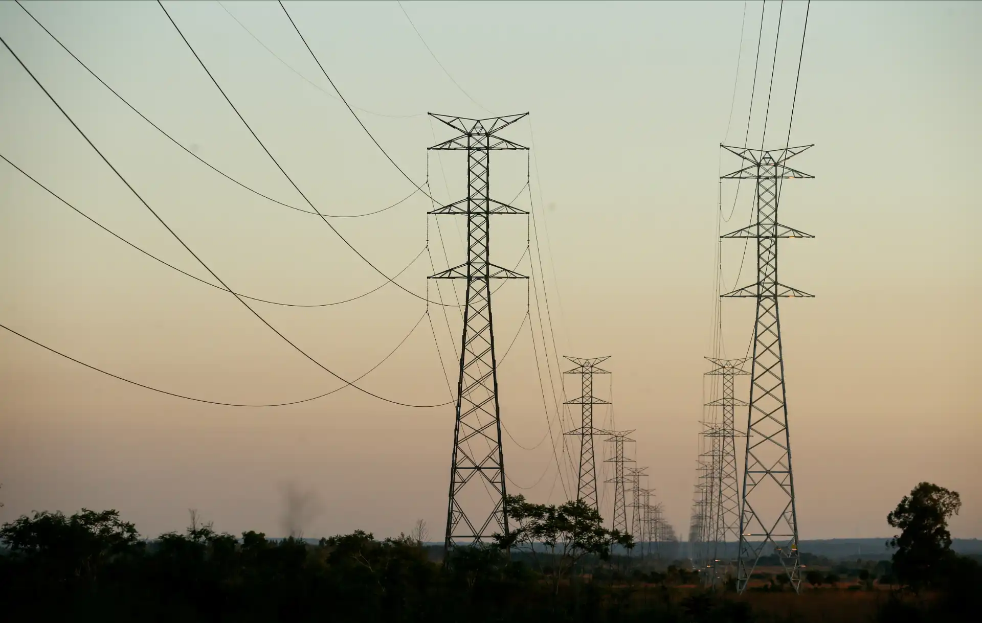 Imagem de torres de transmissão de energia elétrica em um campo aberto durante o pôr do sol, representando a infraestrutura de energia no Brasil.