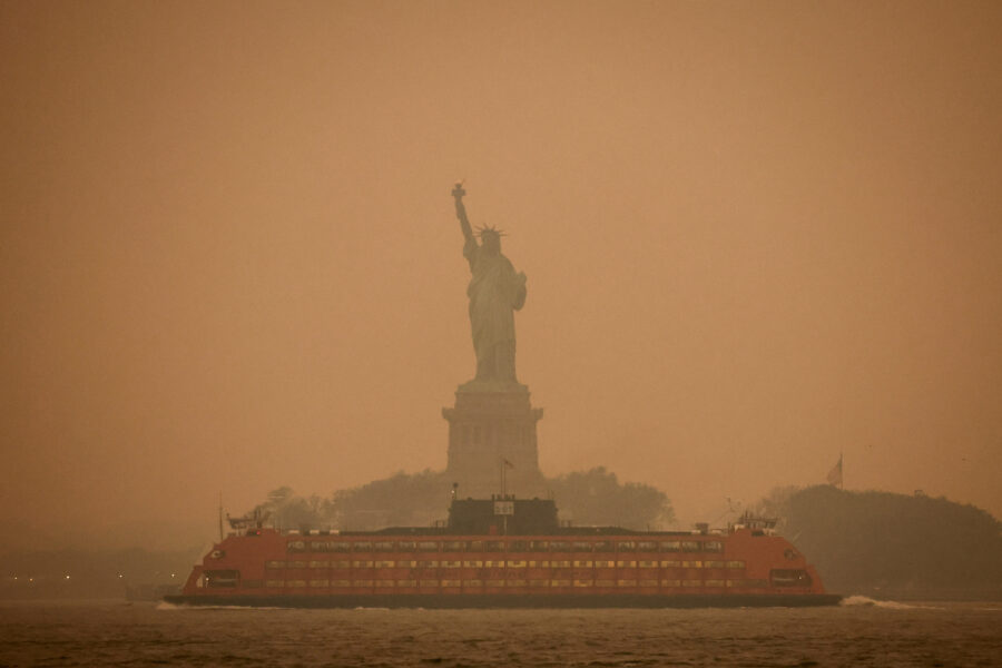 Estátua da Liberdade em meio a neblina, com um barco laranja passando em primeiro plano, representando um cenário icônico de Nova York.