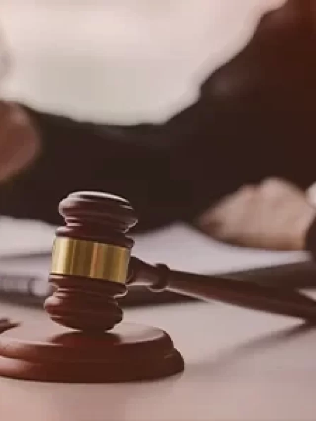 Story Imagem de uma mesa de tribunal com um martelo de juiz em destaque, simbolizando a justiça e discussões legais entre advogados.