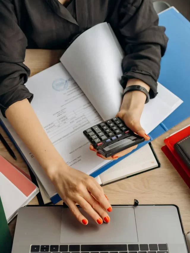 Story Uma mulher utilizando uma calculadora enquanto trabalha em um laptop cercada por documentos e material de escritório, ideal para ambientes de trabalho e produtividade.