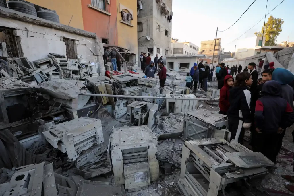 Imagem de um local devastado por destruição, com pessoas ao redor de sucata e destroços, simbolizando a triste realidade de áreas afetadas por conflitos ou desastres.