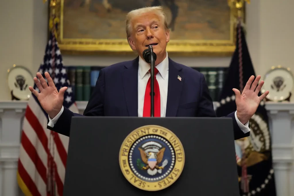 Donald Trump em uma conferência, com a bandeira dos EUA ao fundo. O ex-presidente expressa seu ponto de vista enquanto fala.