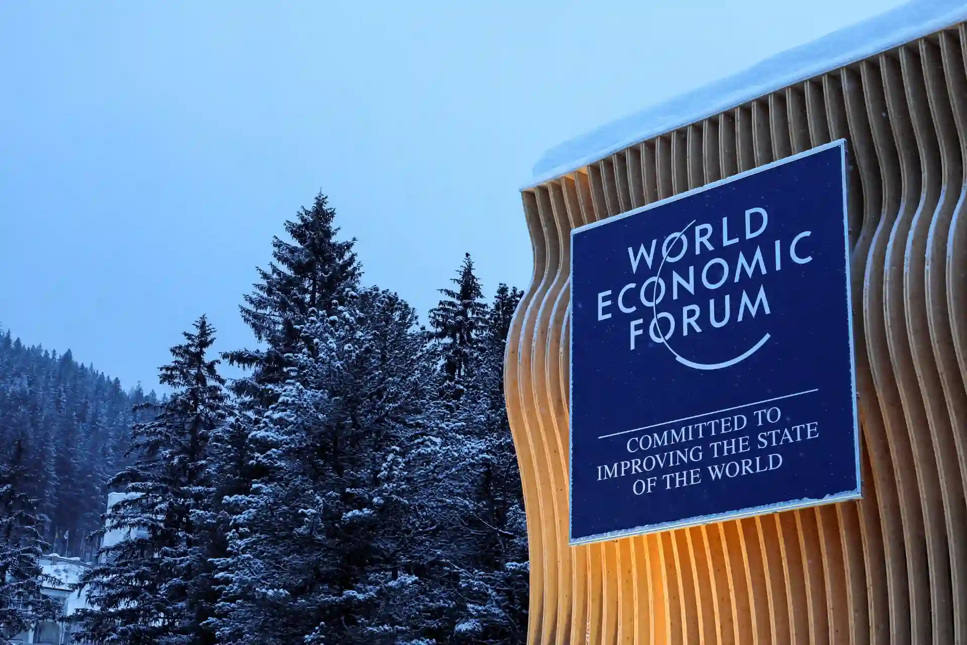 Imagem do Fórum Econômico Mundial em um ambiente coberto de neve, refletindo seu compromisso com a melhoria global. Uma estrutura moderna com a logo em destaque.