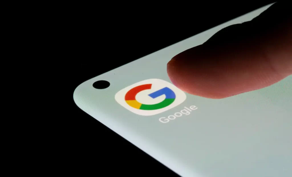 Imagem de um dedo prestes a tocar o ícone do Google em um smartphone, representando interação digital e tecnologia moderna.