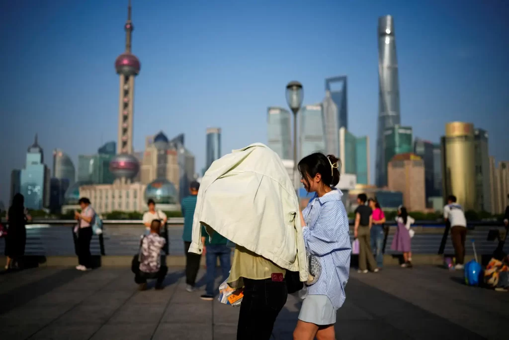 Pessoas interagindo em uma área pública de Xangai, com arranha-céus ao fundo e uma atmosfera vibrante. A cena captura a vida urbana na China moderna.