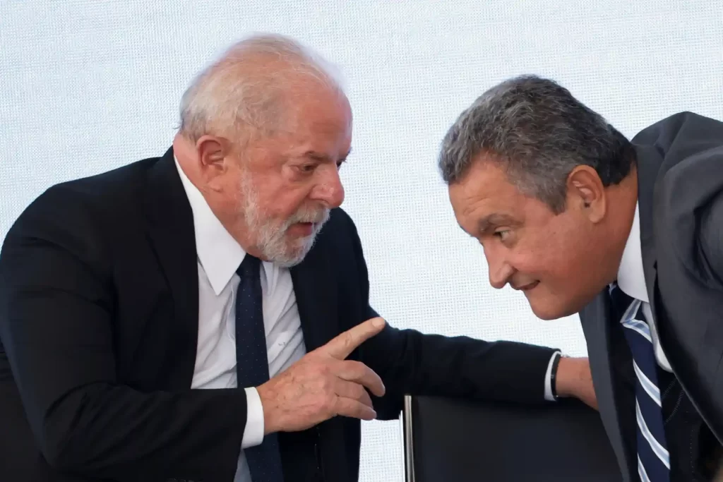 Lula e Rui Costa em uma conversa intensa durante um evento, demonstrando interação e diálogo político.