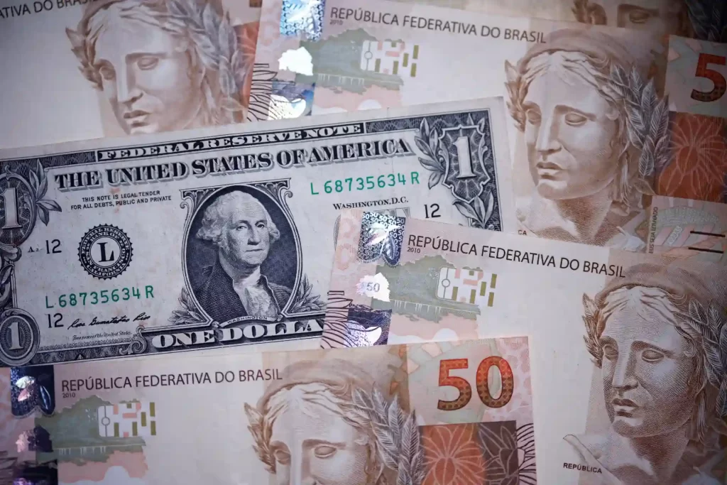 Imagem de notas de dinheiro, incluindo um dólar americano e cédulas da República Federativa do Brasil, representando troca de moedas.