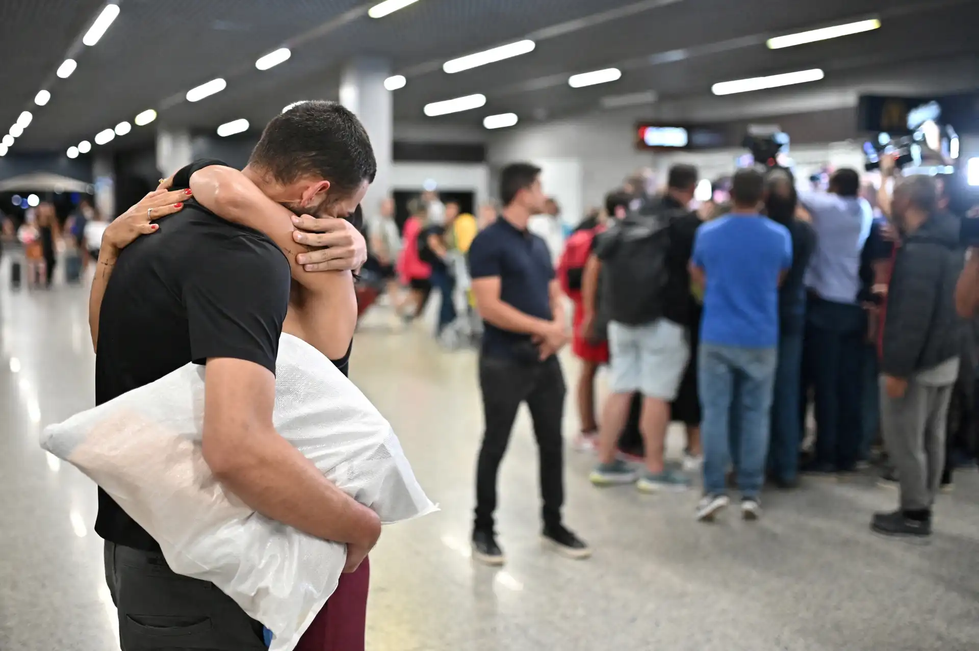 Casal se abraçando no aeroporto, símbolo de reencontro e amor. O sentimento é evidente no ambiente movimentado, com outras pessoas ao fundo.