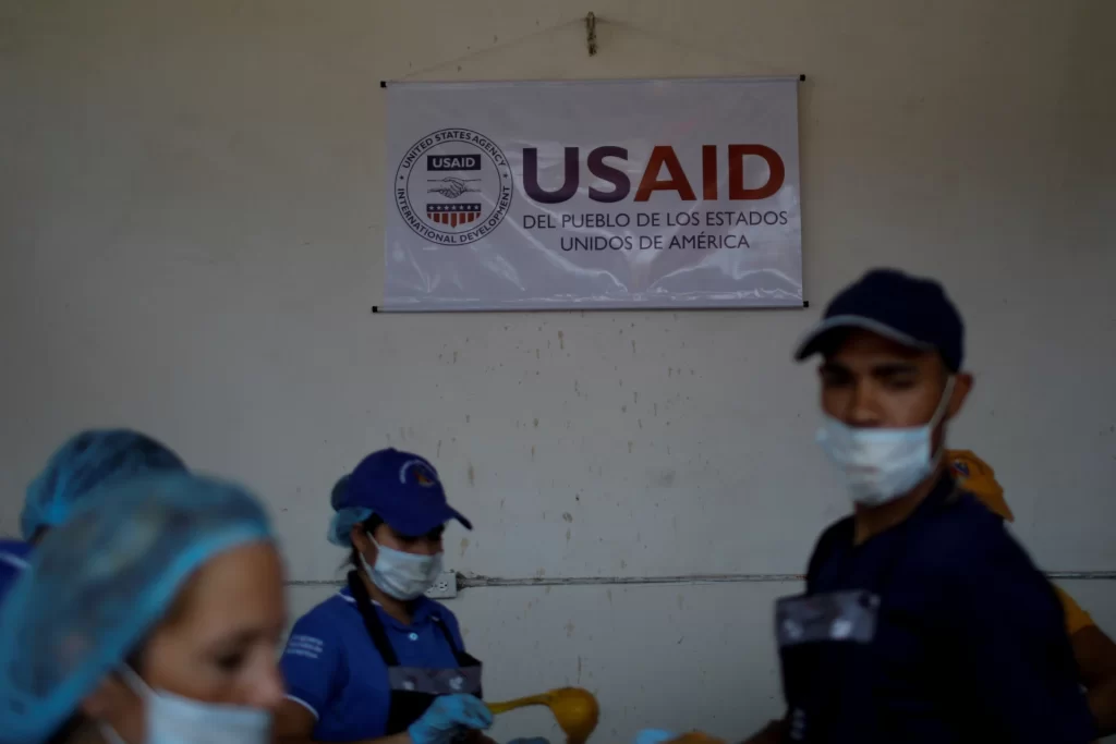 Imagem mostrando trabalhadores voluntários usando equipamentos de proteção durante uma atividade da USAID na comunidade, destacando a importância da ajuda humanitária.