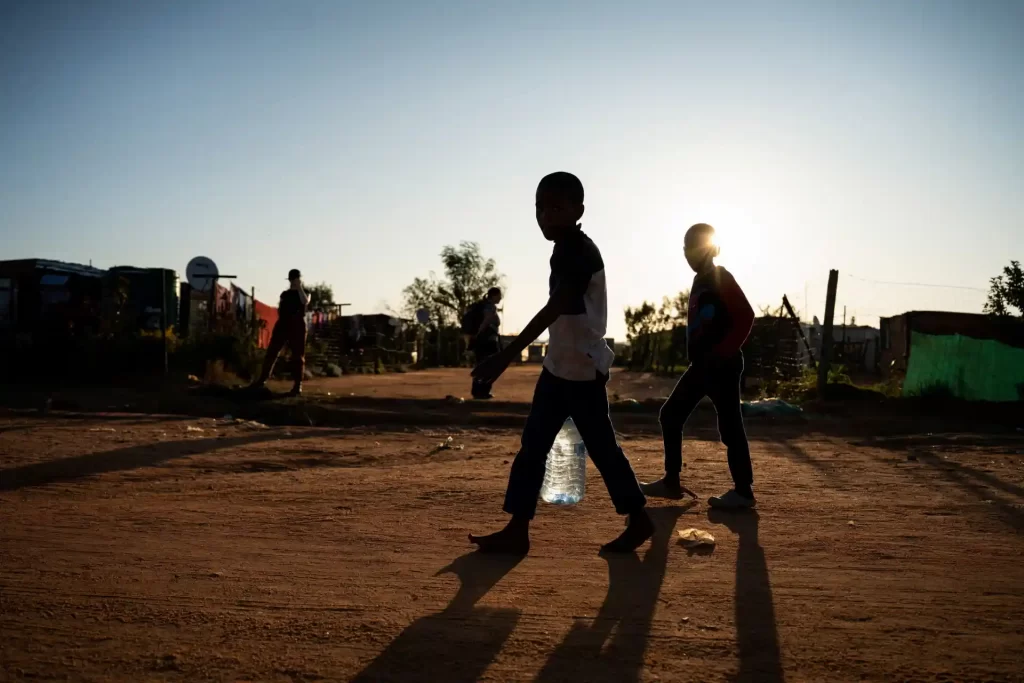 Crianças caminhando em uma rua de terra ao pôr do sol, destacando a vida cotidiana em um ambiente comunitário. Imagem que retrata a simplicidade e a esperança.