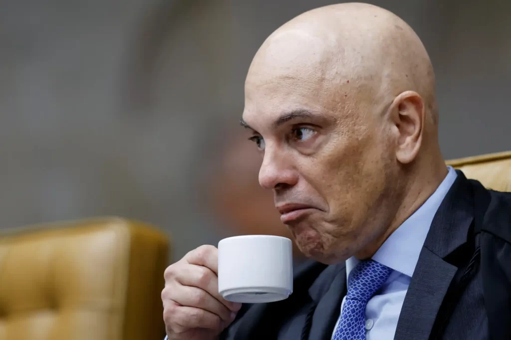 Imagem de um homem segurando uma xícara de café, com expressão pensativa, em ambiente formal de tribunal.