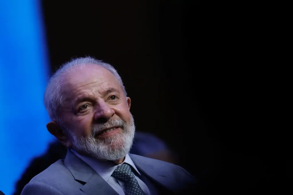 Lula da Silva em evento, sorrindo e mostrando seu entusiasmo, enquanto é iluminado por luz azul ao fundo, representando seu papel na política brasileira.
