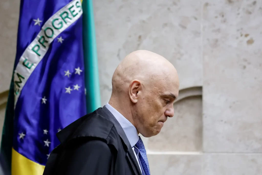 A imagem mostra um magistrado brasileiro com expressão séria, em frente à bandeira do Brasil. O cenário reflete o ambiente do judiciário nacional.