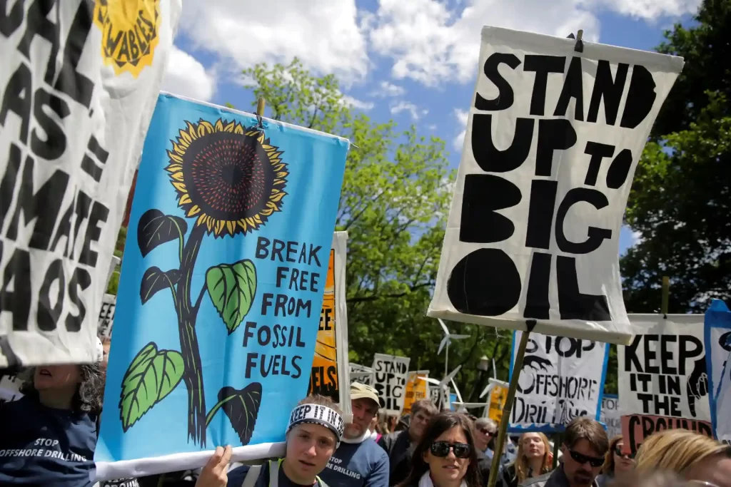 Manifestação contra combustíveis fósseis com cartazes inspiradores, destacando a luta por energias renováveis e a proteção ao meio ambiente.