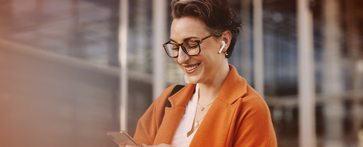 Mulher sorridente usando fones de ouvido sem fio e consultando smartphone, destacando tendência de tecnologia e estilo moderno. Ela está em um ambiente moderno, perfeito para ilustrar a conexão com a inovação e lançamentos