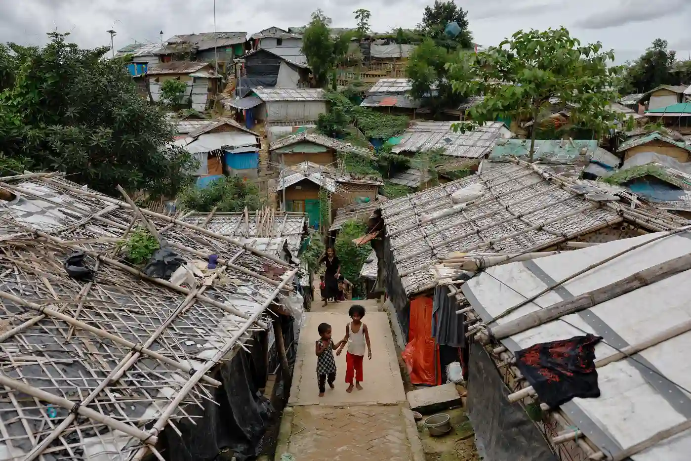 Imagem de crianças caminhando em um assentamento informal, rodeadas por casas de telhado de palha e madeira, representando a realidade das comunidades em áreas de vulnerabilidade social.