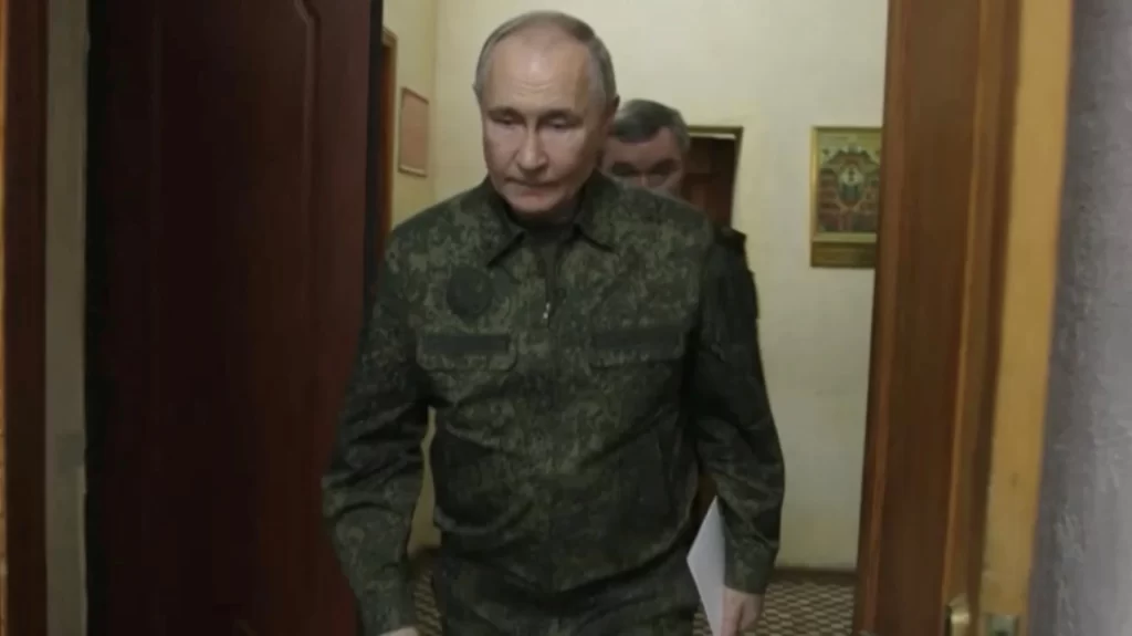 Vladimir Putin em uniforme militar, caminhando no interior de um edifício. A imagem retrata uma atmosfera séria e focada.