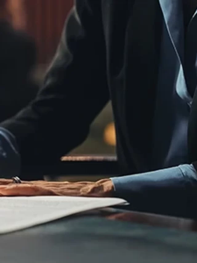 Story Imagem de um profissional escrevendo documentos em uma mesa, com copo de água ao lado e ambiente de escritório ao fundo, destacando a importância da escrita em negociações.