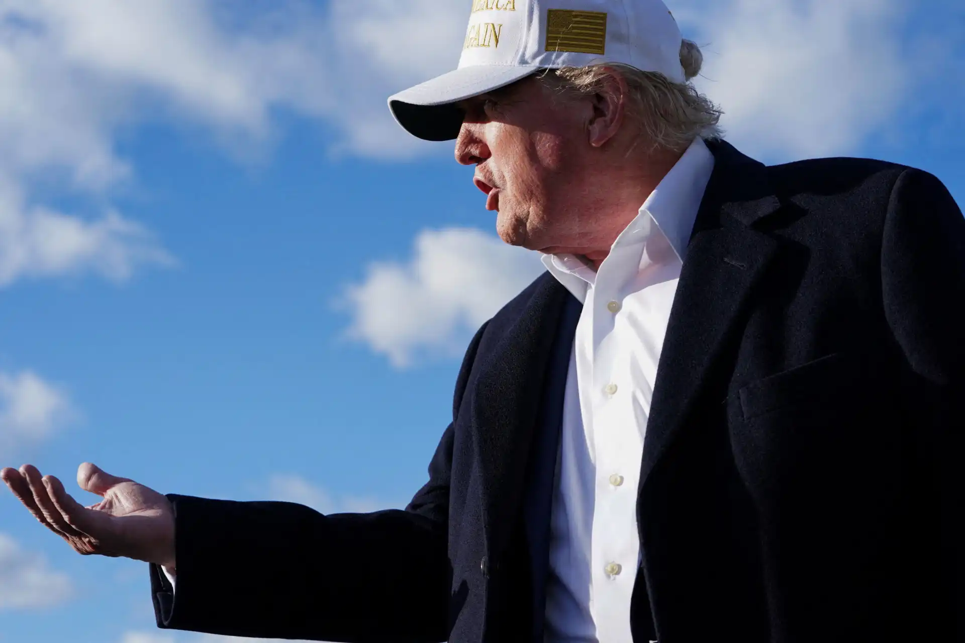 Imagem de Donald Trump em discurso, vestido com blazer e boné, gesticulando sob um céu azul com nuvens. Captura um momento de eloquência e carisma.