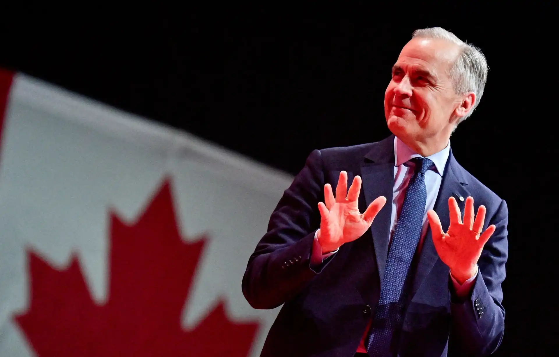 Imagem de um homem sorridente gesticulando em frente a uma bandeira do Canadá, destacando sua conexão com o país.