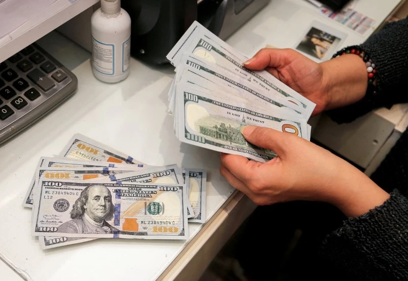 Pessoa contando cédulas de dólar em uma mesa, evidenciando a importância do dinheiro nas transações cotidianas. A imagem retrata a realidade financeira e a gestão de recursos.