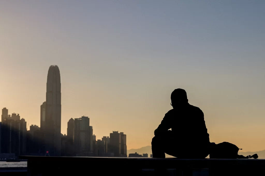 Silhueta de uma pessoa contemplando a cidade ao pôr do sol, com arranha-céus ao fundo. Uma cena tranquila que transmite paz e reflexão. Ideal para ilustrar momentos de introspecção e urbanidade.