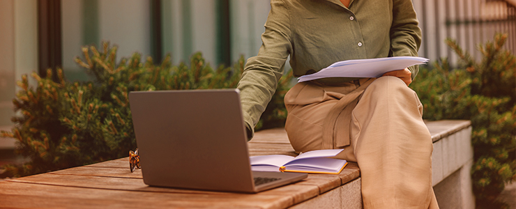 Pessoa trabalhando ao ar livre com laptop, pasta e cadernos na mão. Ambiente tranquilo e produtivo, ideal para estudos e trabalho remoto com os lançamentos de maio de 2025