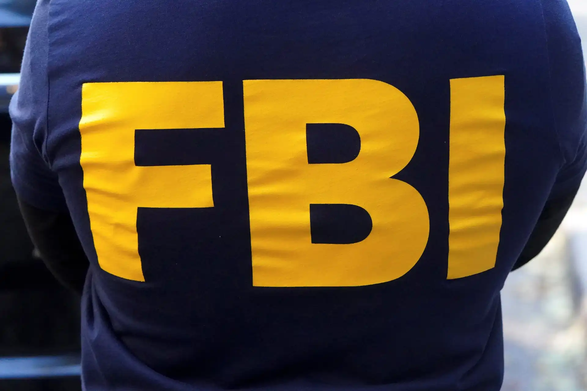 Agente do FBI com uniforme azul exibindo letras amarelas em destaque. A imagem retrata a vitalidade da missão do FBI na segurança pública.