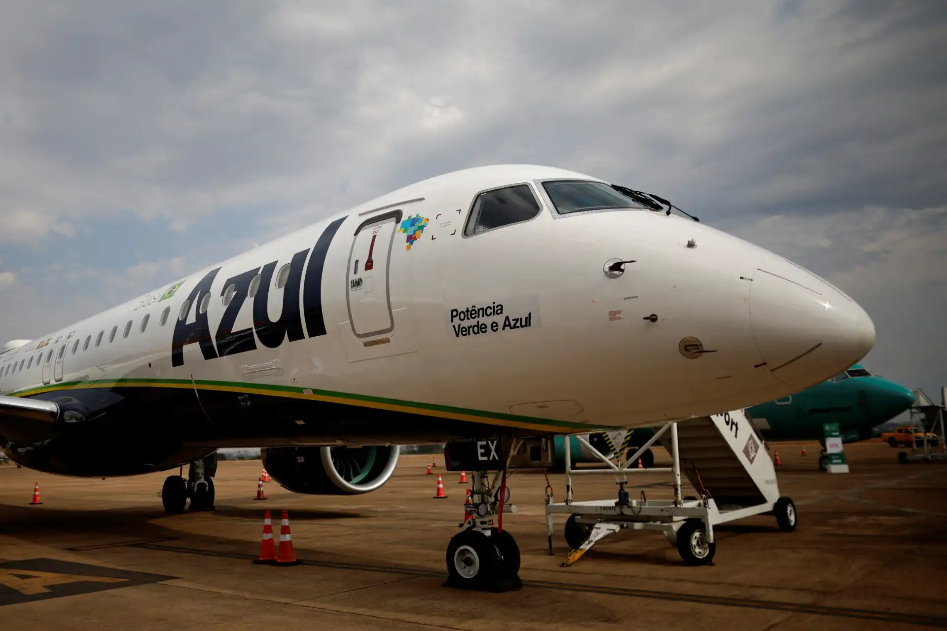 Avião da Azul Linhas Aéreas no aeroporto, com destaque para a marca Azul e a frase Potência Verde e Azul, com um céu nublado ao fundo.