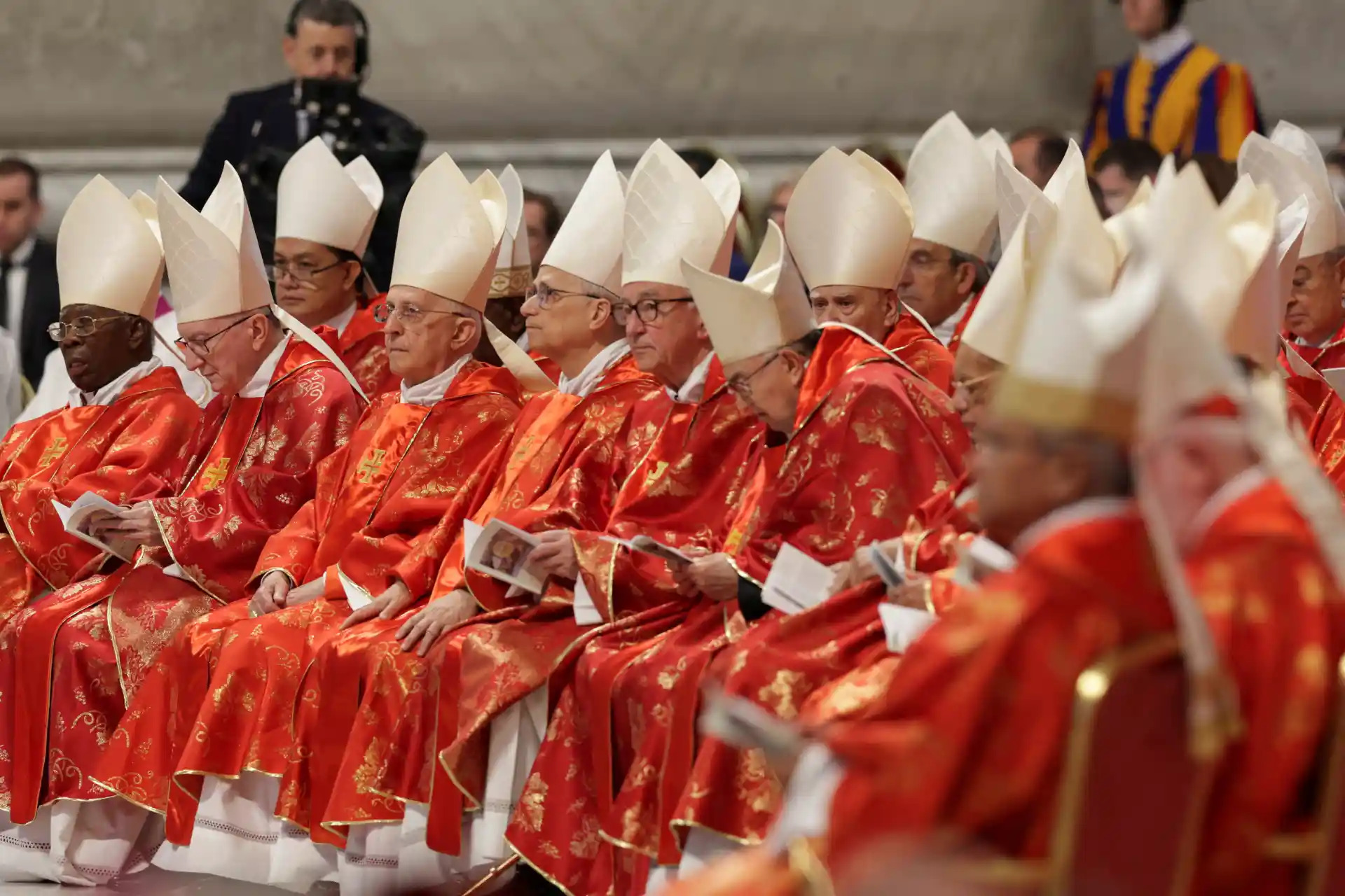 Cerimônia religiosa com cardeais em trajes vermelhos e chapéus brancos, refletindo tradições católicas no Vaticano.