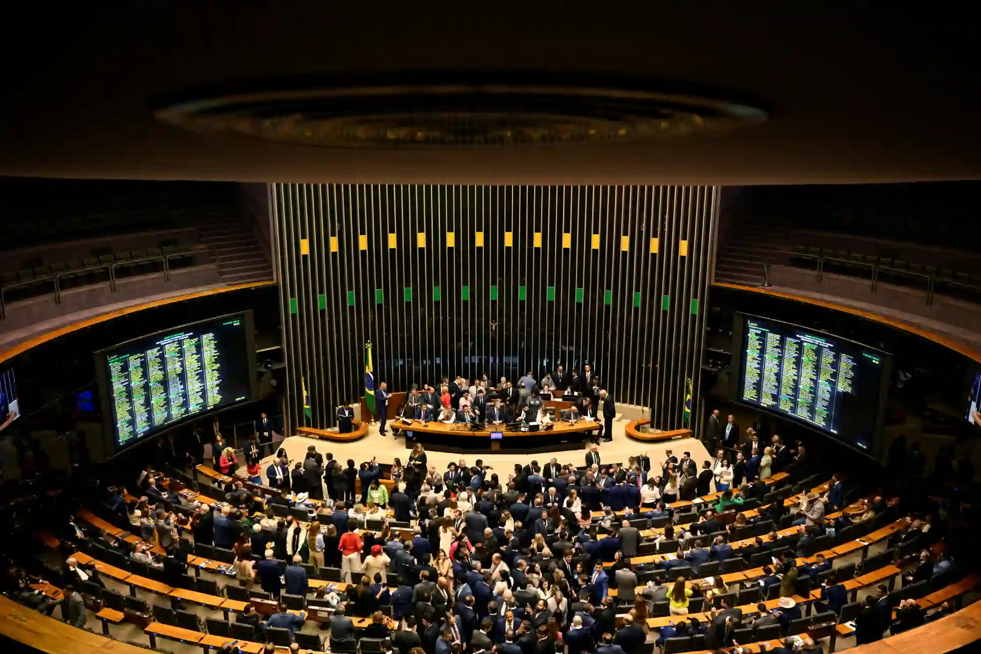 Imagem do Congresso Nacional do Brasil durante uma sessão com muitos deputados e funcionamento dos painéis eletrônicos, simbolizando a democracia e a atividade legislativa.