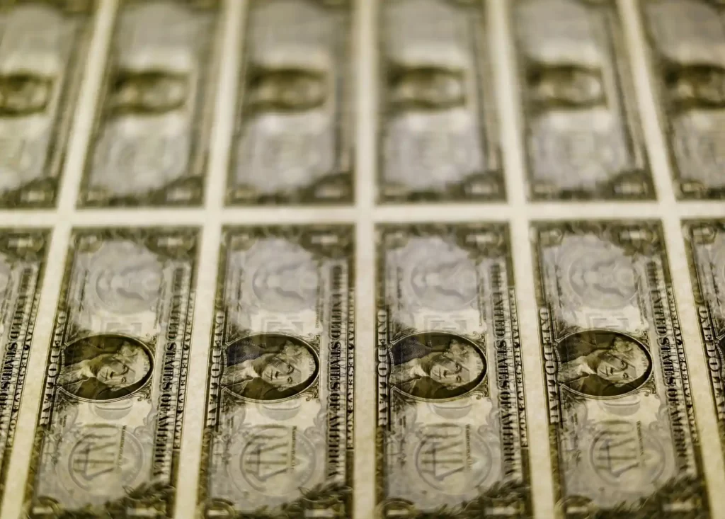 Vários dólares americanos, em papel moeda, dispostos em linhas, representando valores financeiros e economia.