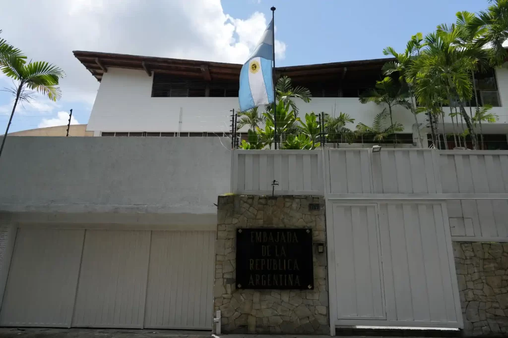 Imagem da Embaixada da República Argentina, destacando a bandeira argentina e a arquitetura do edifício com vegetação ao redor.