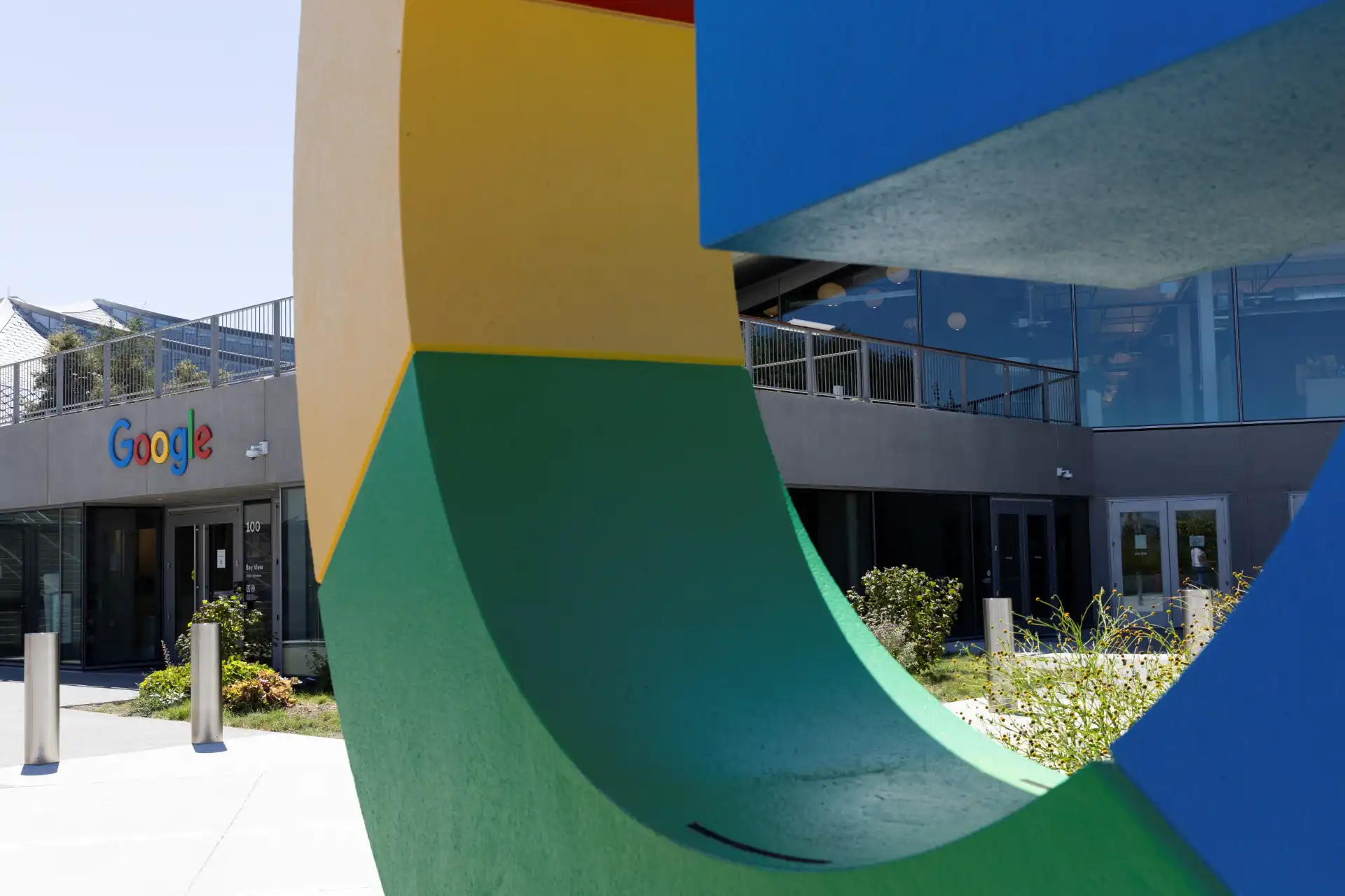 Imagem da fachada do escritório do Google, com estrutura colorida e moderna, destacando o logotipo da empresa em um dia ensolarado.