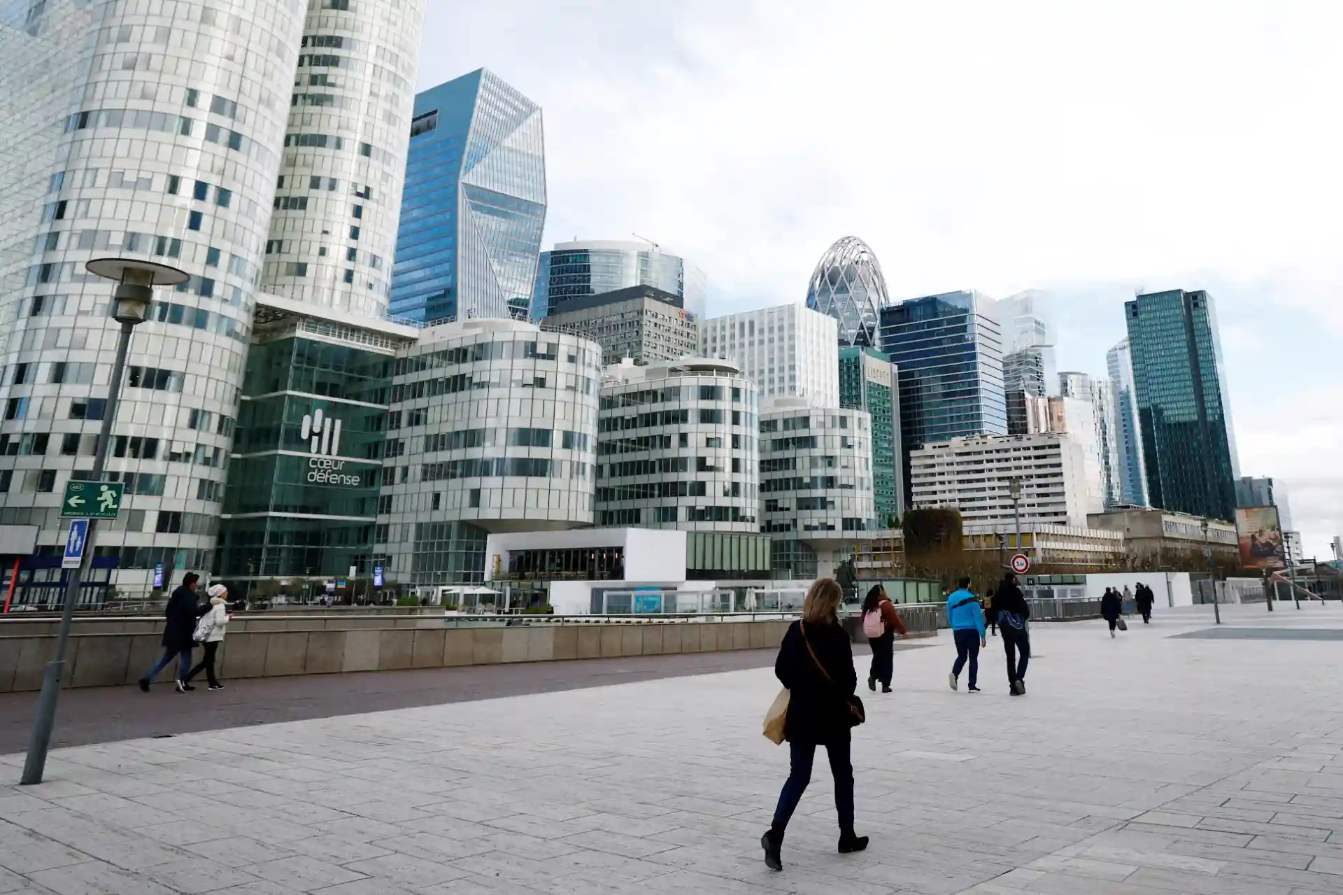 Vista urbana moderna de La Défense, com edifícios de escritórios e pessoas caminhando pela calçada, simbolizando a vitalidade do centro financeiro.