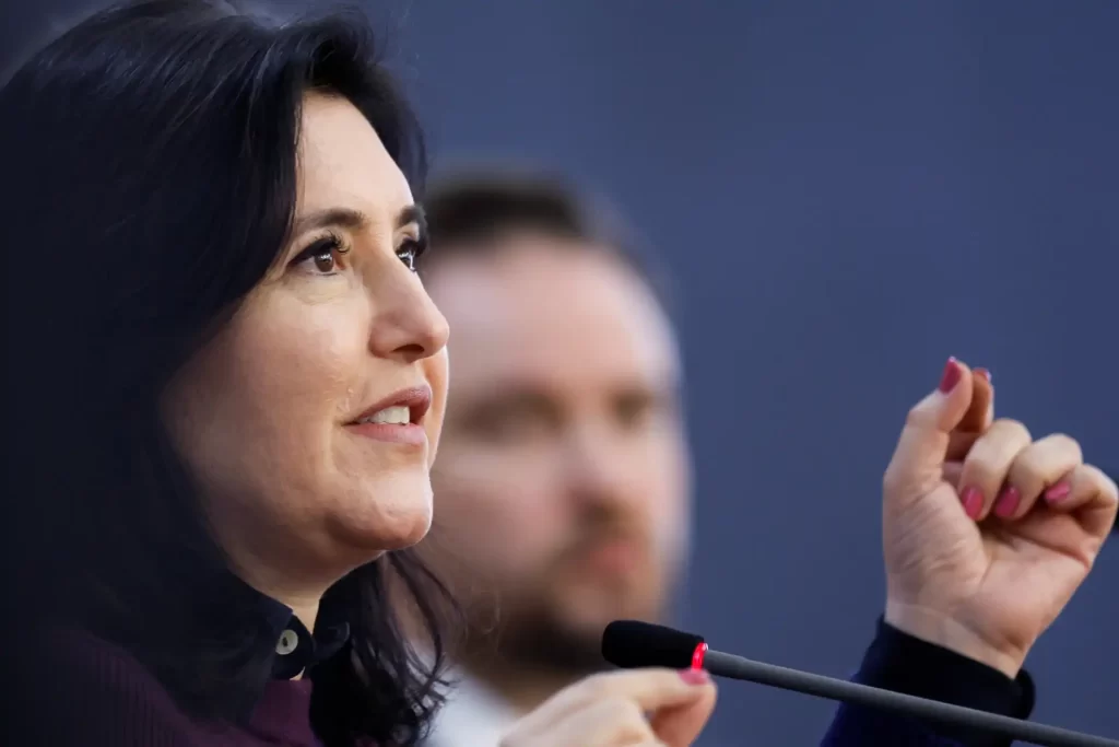 Imagem de uma mulher falando em um microfone durante uma apresentação, com expressão confiante e envolvente, emitindo uma mensagem clara e assertiva.