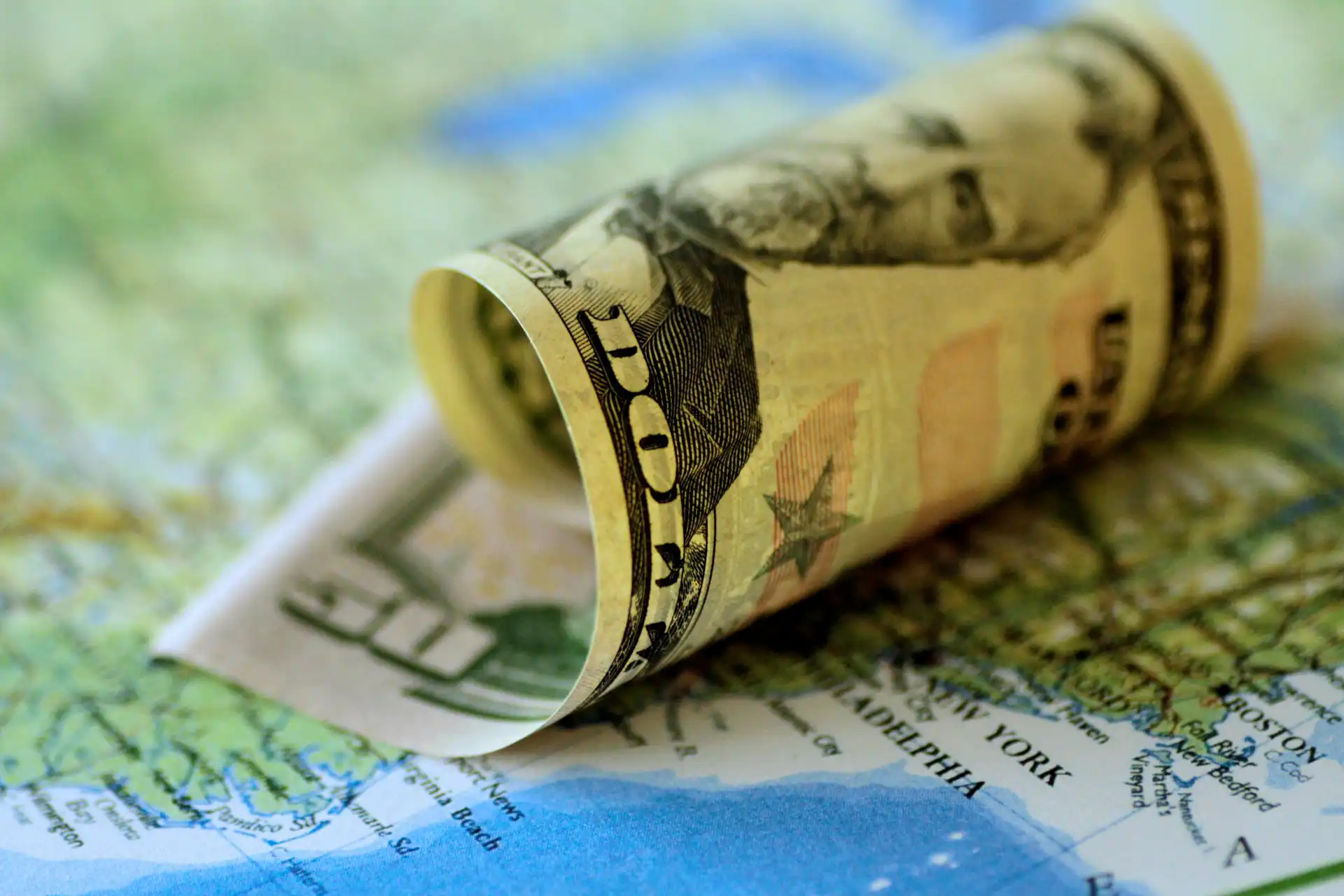 Notas de cem dólares roladas sobre um mapa, simbolizando finanças e investimentos.
