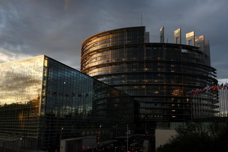 Imagem do Parlamento Europeu em Estrasburgo, destacando sua arquitetura moderna e as bandeiras de países membros ao lado.