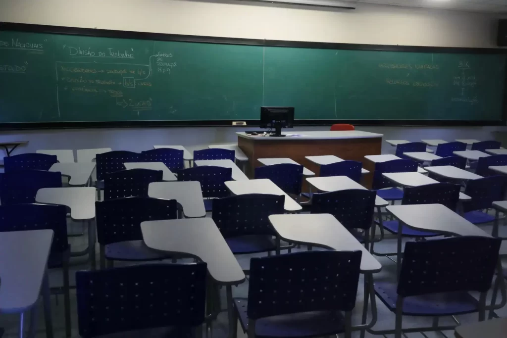 Sala de aula vazia com carteiras e quadro-negro, ambiente escolar preparado para aulas presenciais de ensino.