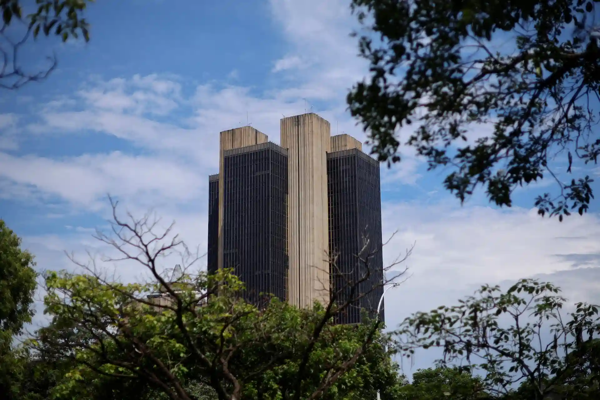 Imagem do edifício Torre de São Paulo visto de frente com árvores ao redor e céu claro ao fundo, representando arquitetura moderna.