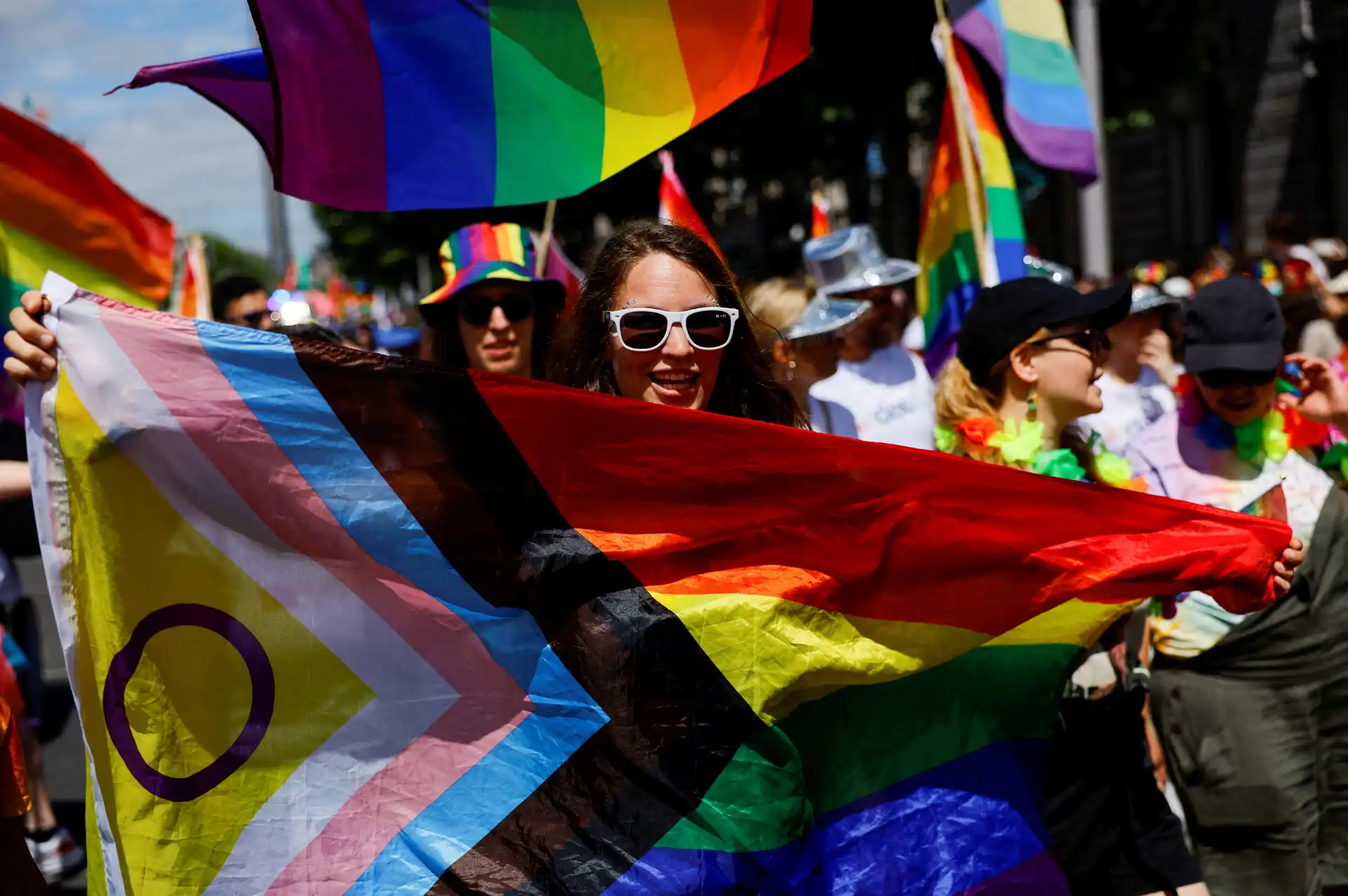 Pessoas celebrando o Dia do Orgulho LGBTQ+ com bandeiras coloridas e roupas vibrantes em uma marcha, demonstrando orgulho e diversidade.