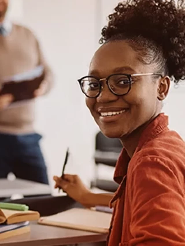 Story Estudante sorridente em sala de aula com colegas estudando ao fundo, demonstrando entusiasmo e conhecimento na sala de aula, ideal para artigos sobre educação e estudantes.