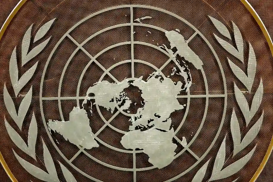 Emblema da Organização das Nações Unidas (ONU) mostrando o mapa-múndi no centro, rodeado por ramos de oliveira, simbolizando paz e cooperação internacional.