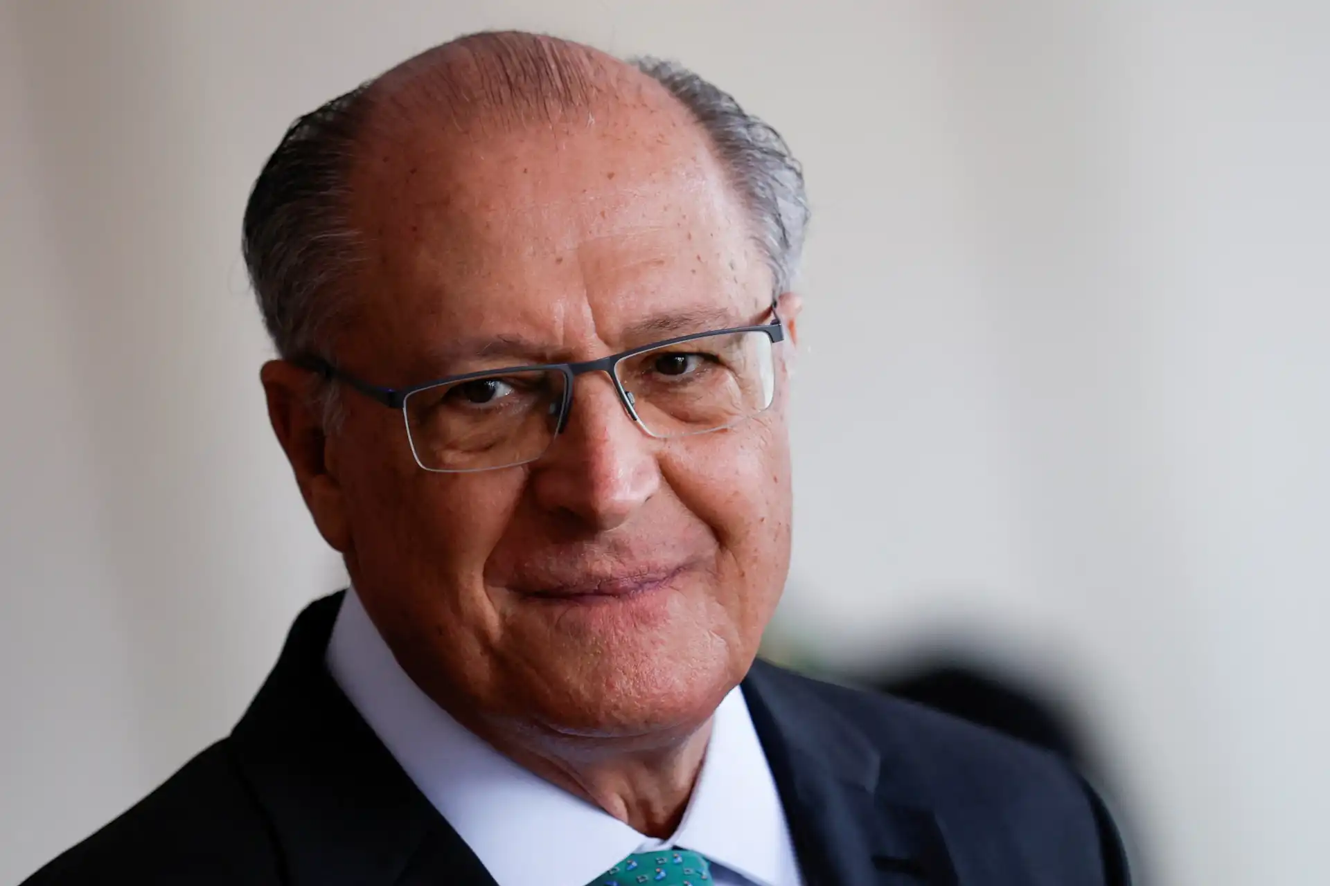 Imagem de um homem idoso, com cabelos grisalhos, vestindo terno e gravata, sorrindo e usando óculos, representando uma figura de autoridade ou liderança.