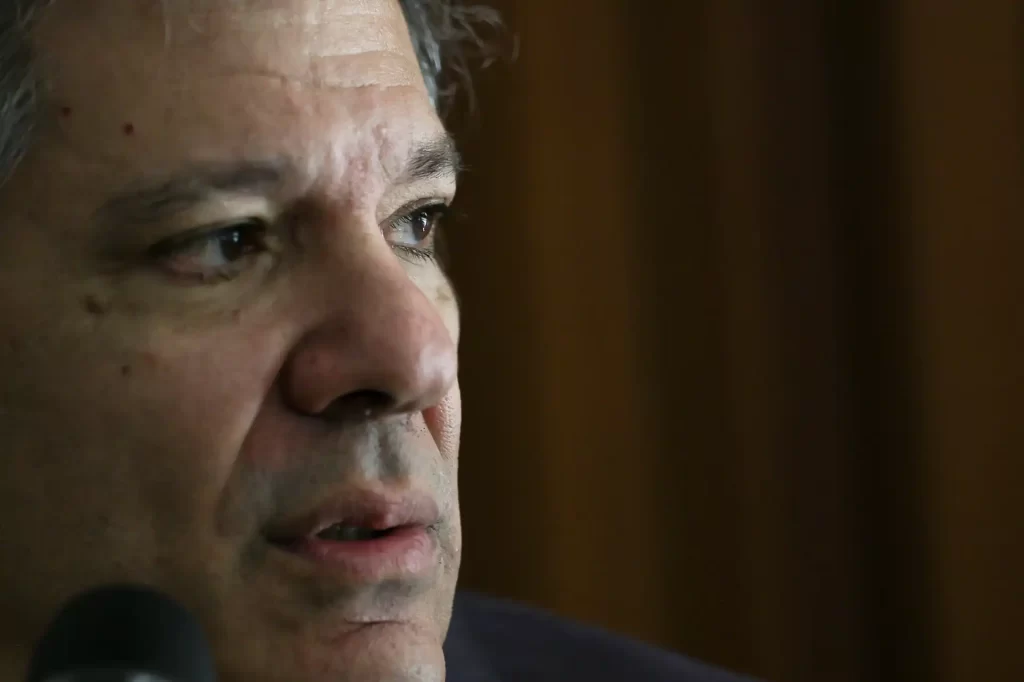 Close-up da face de um homem sério e pensativo, com expressão de concentração, em ambiente interno com fundo escuro.